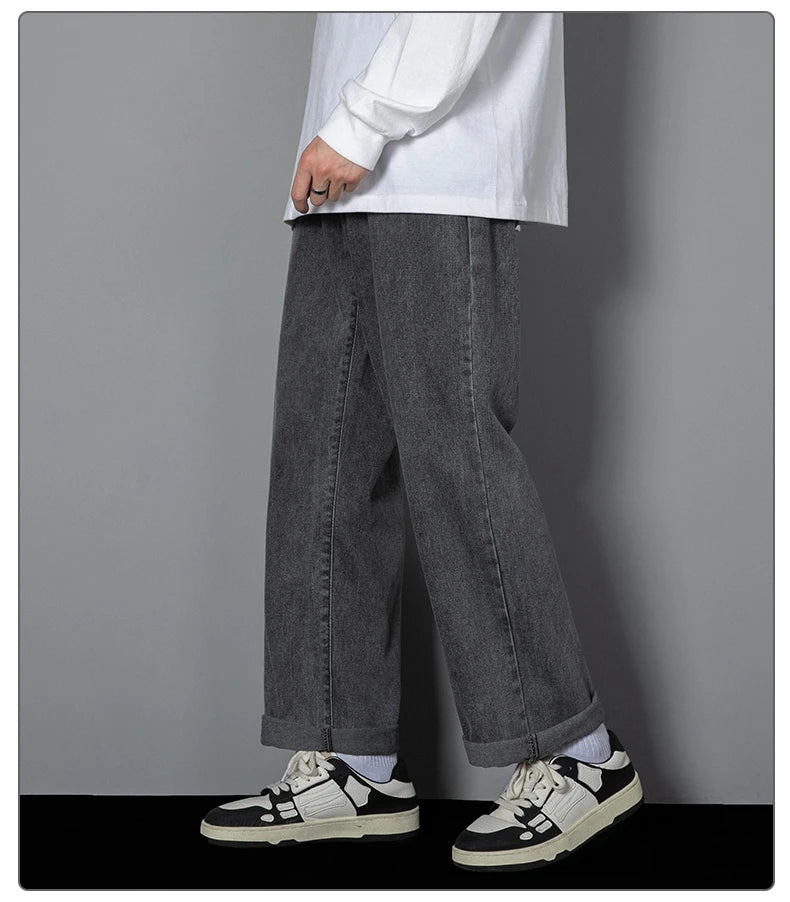 Person wearing dark gray wide-leg jeans and black and white sneakers on a plain background