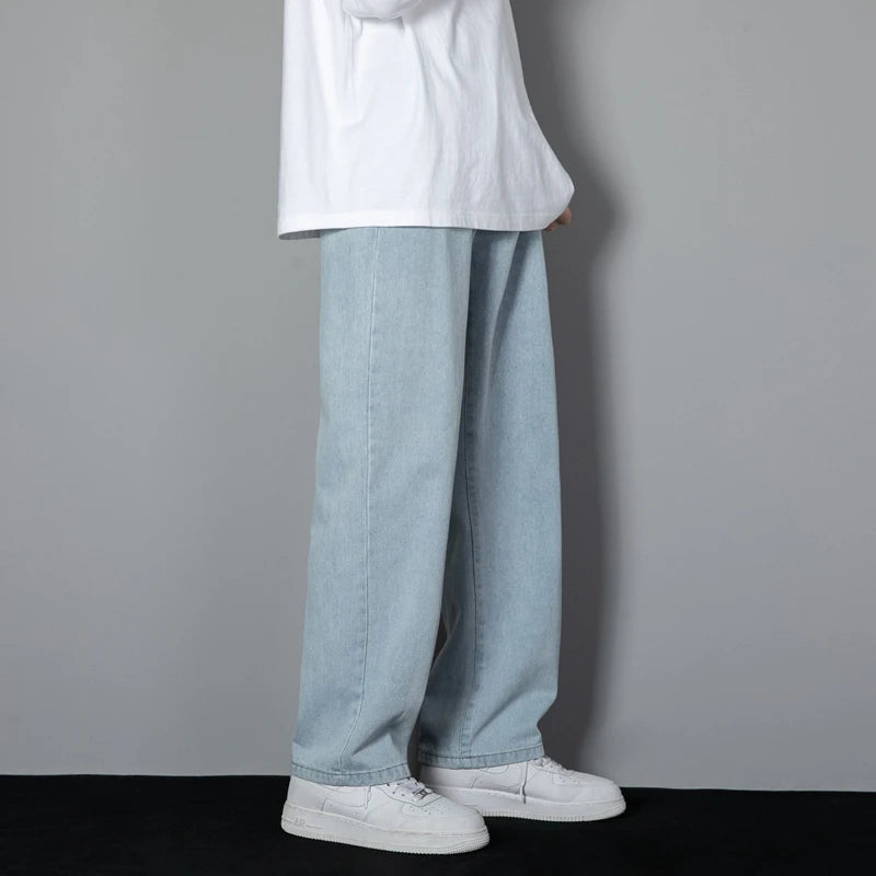 Person wearing light blue jeans and white sneakers against a gray background
