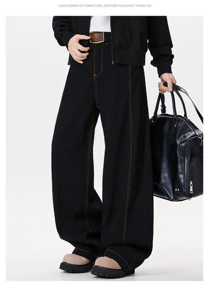 Person wearing black wide-leg pants holding a black bag on a white background
