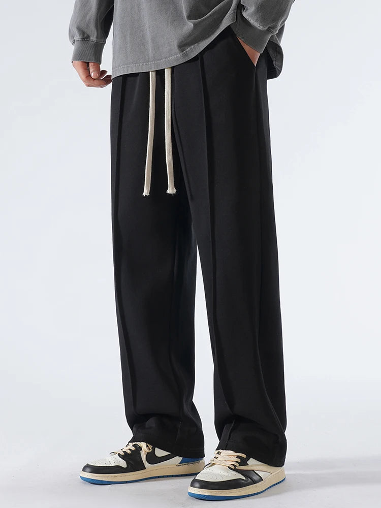 Person wearing black wide-leg pants with a gray top and white sneakers on a light gray background