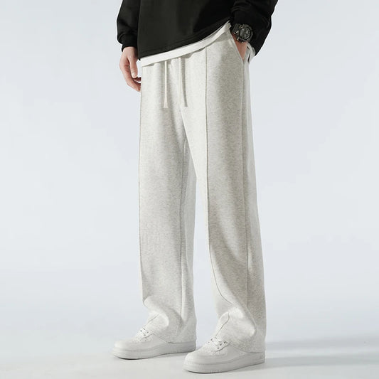 Person wearing light gray sweatpants and white sneakers on a plain background